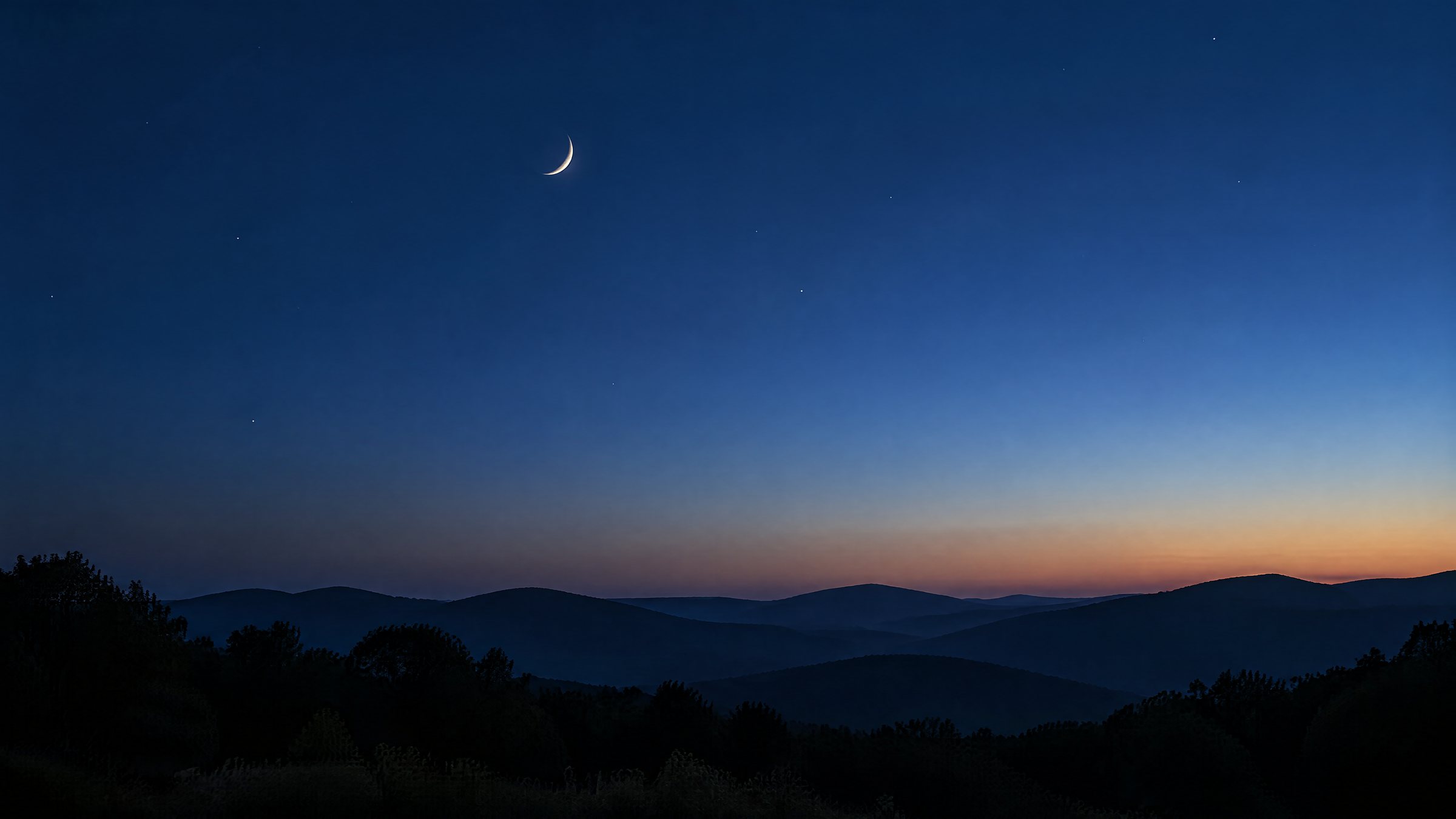 A quiet night sky over a low horizon at blue hour, with a thin crescent moon